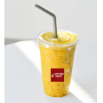 A mango smoothie in a clear plastic cup with a dome lid and a gray straw, labeled "Bamboo House Boba Cafe," is placed on a white surface.