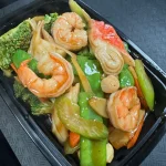 A black tray containing cooked shrimp, broccoli, snow peas, onions, and carrots mixed together.