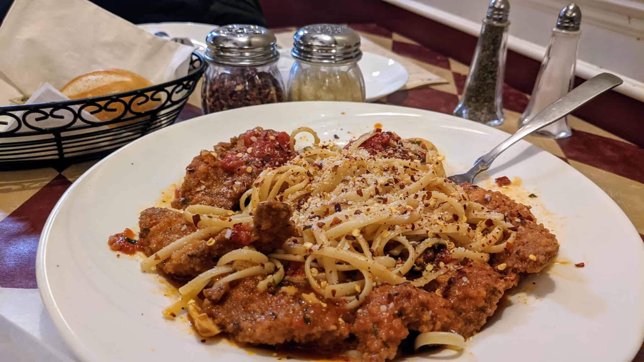 Spaghetti dish with a piece of bread behind it on a table.