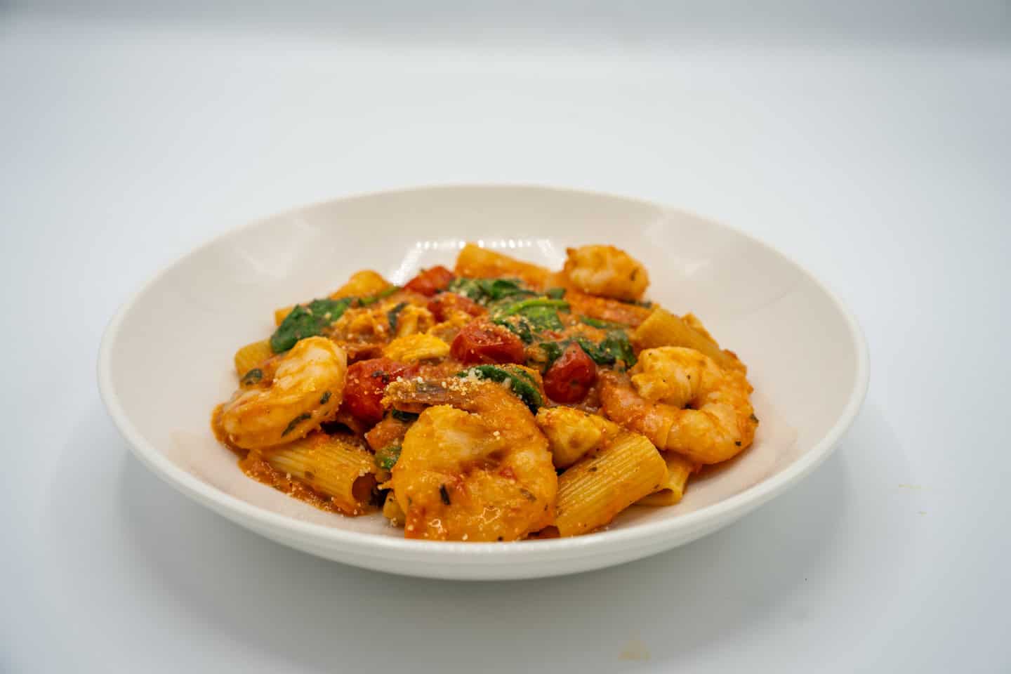 A plate of pasta with shrimp, spinach, and cherry tomatoes in a creamy sauce, presented on a white background.