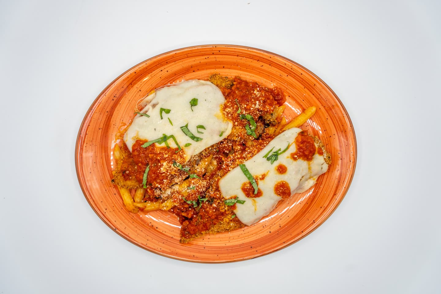 A plate of penne pasta with marinara sauce, garnished with melted cheese and chopped herbs, on an orange plate against a white background.