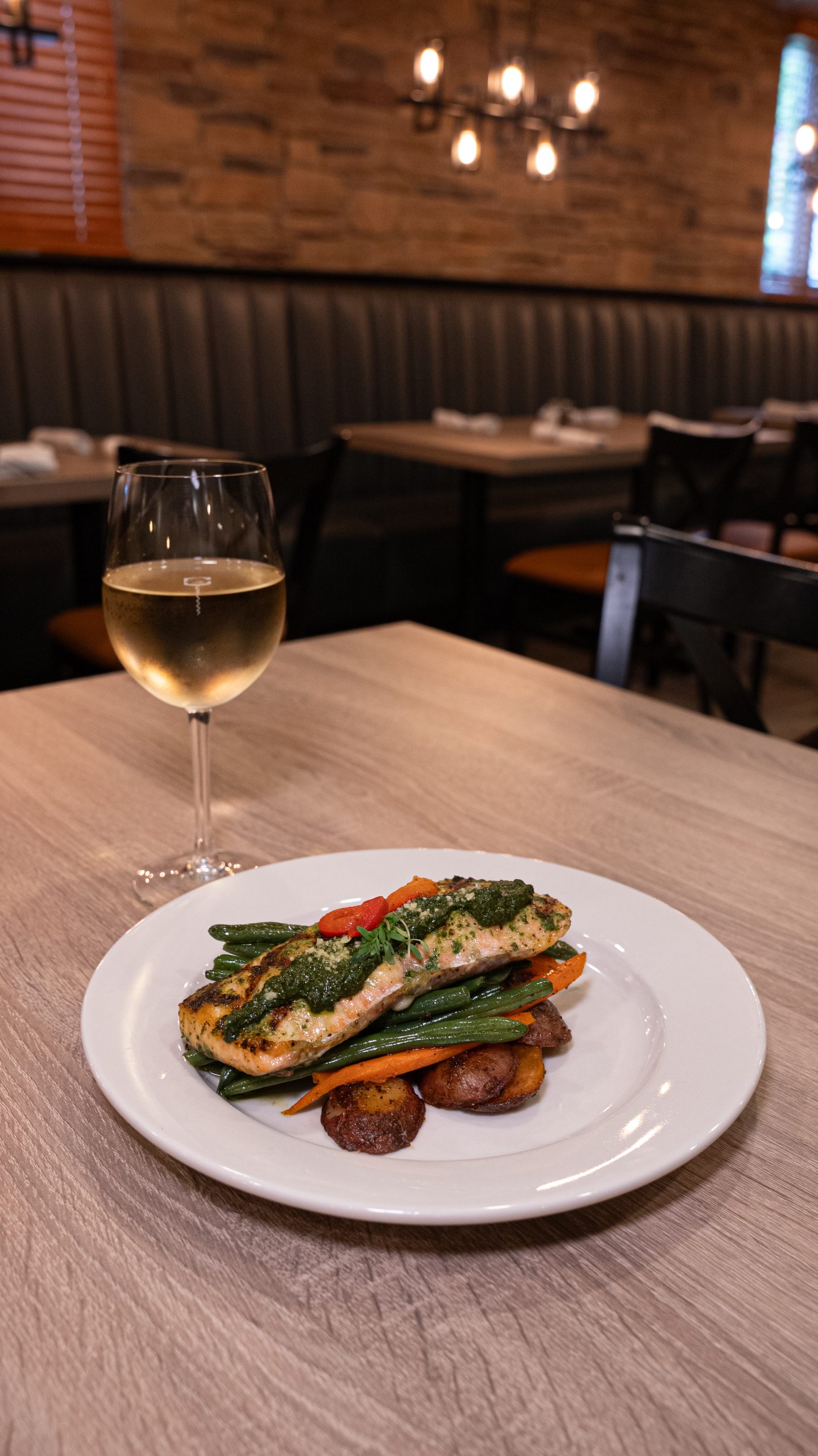 A plated dish featuring a fish fillet with vegetables and roasted potatoes, accompanied by a glass of white wine on a restaurant table.