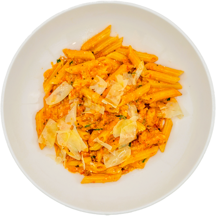 A white bowl contains penne pasta coated in a creamy orange sauce, garnished with shaved cheese and herbs.