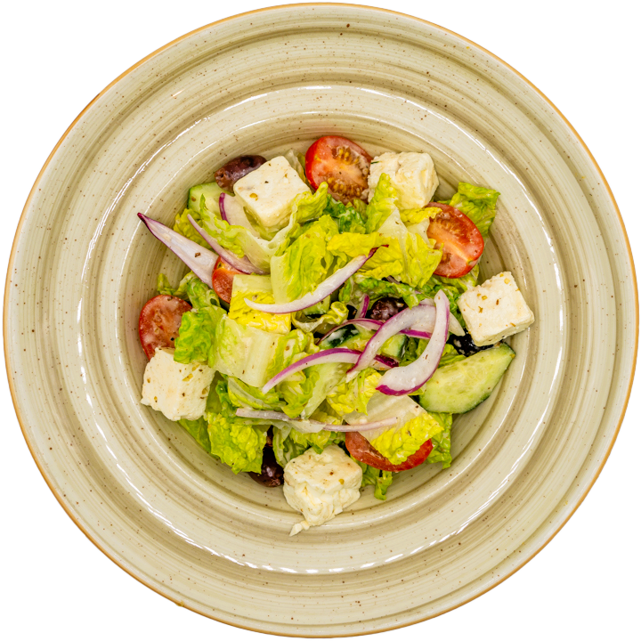 A bowl of Greek salad with lettuce, feta cheese, cherry tomatoes, cucumber, black olives, and sliced red onions, arranged in a ceramic dish.