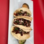 Three tacos on a plate with guacamole and salsa.