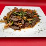 A plate of beef and vegetables on a red plate.