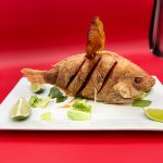 A fried fish on a plate with lime wedges.