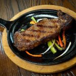 A steak in a skillet on a wooden table.