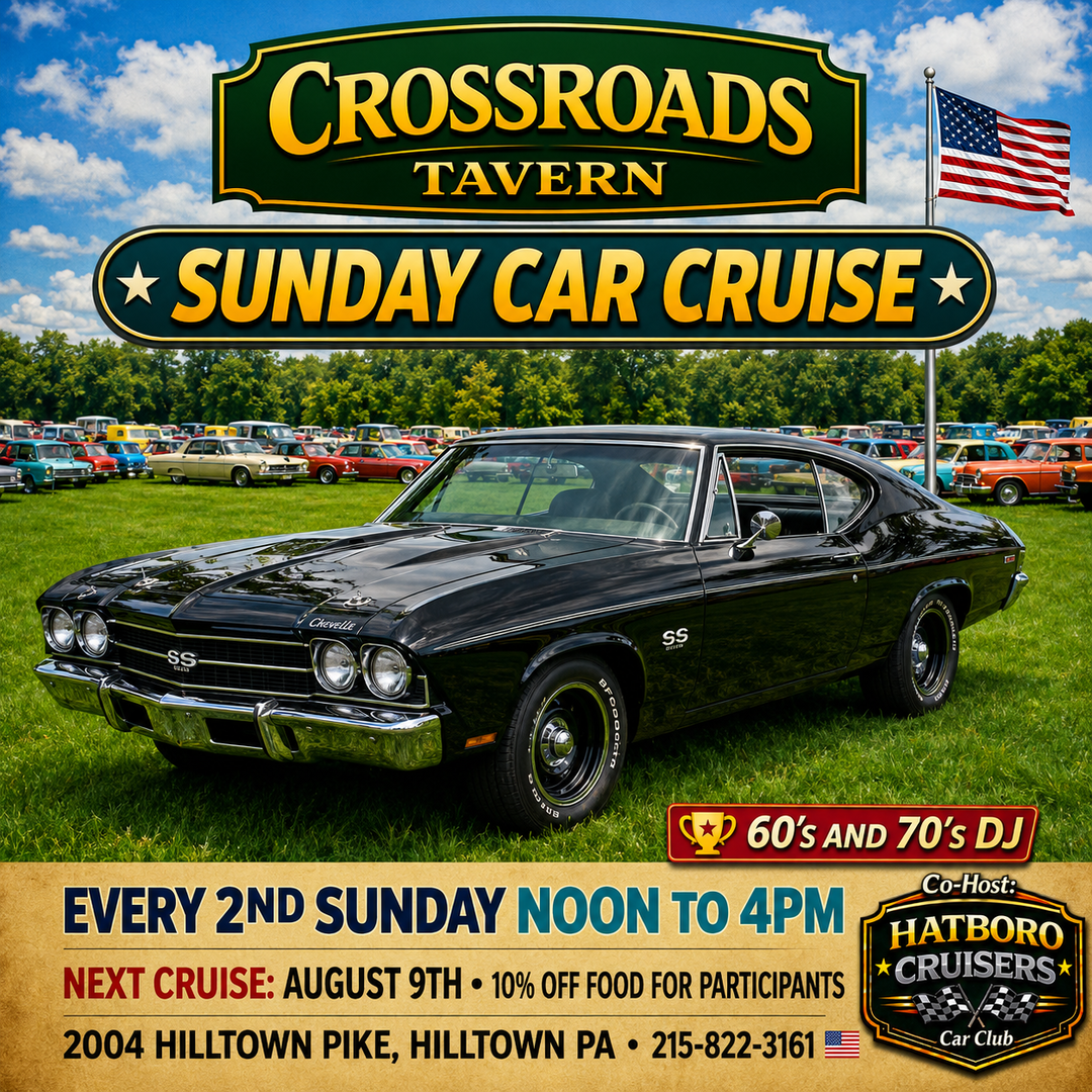 A classic black Chevrolet muscle car parked on grass at a car show event, with promotional signs for Crossroads Tavern Sunday Car Cruise in the background.